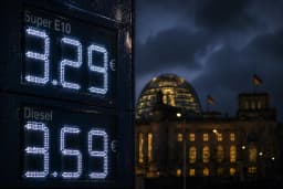 Preisanzeige einer Tankstelle in der Nacht: Super E10 für 3,29 Euro und Diesel für 3,58 Euro pro Liter, im Hintergrund die beleuchtete Kuppel des Berliner Reichstagsgebäudes mit deutscher Flagge unter bewölktem Nachthimmel.